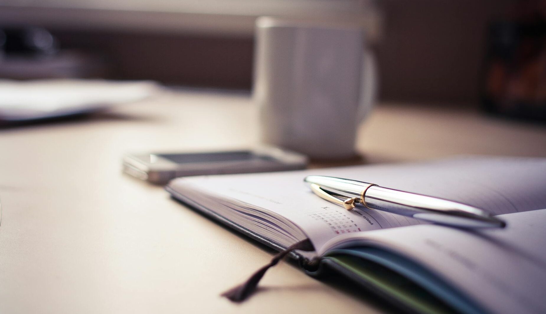 Cozy workspace with an open planner, pen, and coffee mug on a desk.